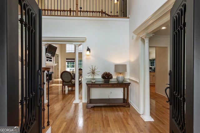 foyer with ornate columns, a towering ceiling, and light wood-style flooring