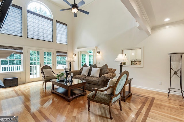 living area with ornamental molding, a towering ceiling, a ceiling fan, healthy amount of natural light, and light wood-style floors