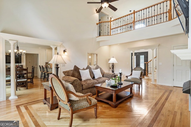 living room featuring a high ceiling, a ceiling fan, light wood-style flooring, a chandelier, and baseboards