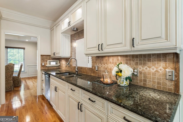 kitchen with a sink, stainless steel dishwasher, light wood finished floors, tasteful backsplash, and dark stone countertops