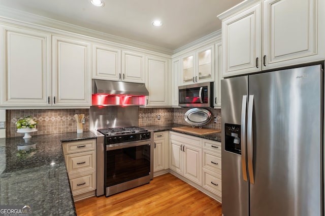kitchen featuring stainless steel appliances, under cabinet range hood, backsplash, light wood-style floors, and dark stone countertops