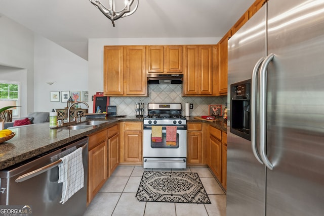 kitchen featuring stainless steel appliances, under cabinet range hood, a sink, decorative backsplash, and dark stone counters