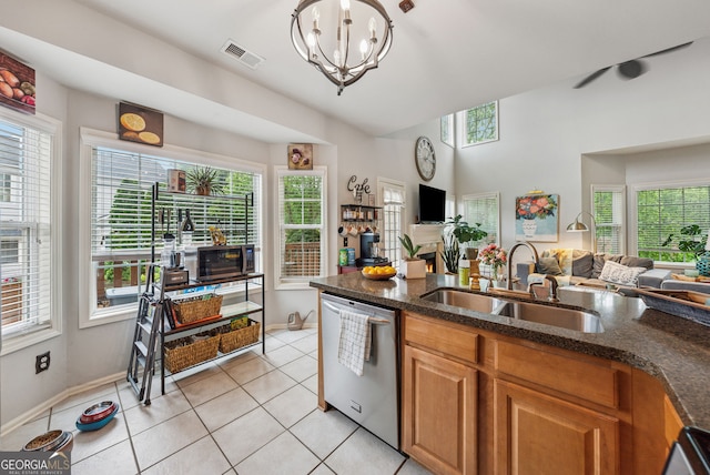 kitchen featuring stainless steel dishwasher, a sink, open floor plan, light tile patterned flooring, and dark stone counters