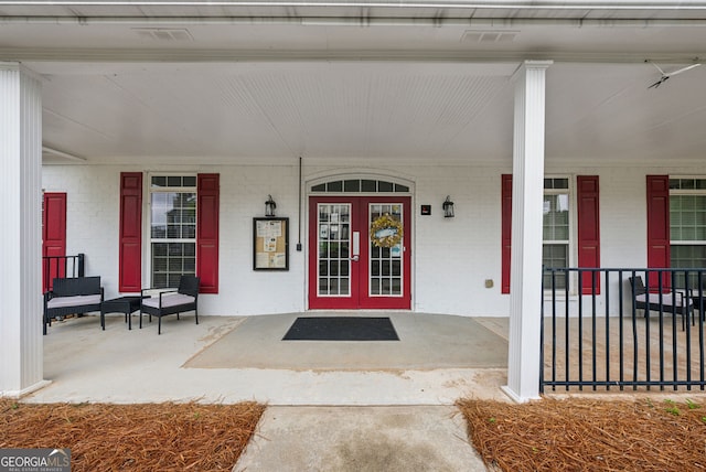 entrance to property featuring covered porch, brick siding, and french doors