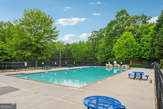 community pool with fence, a patio area, and view of wooded area