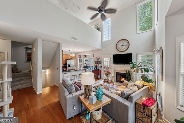 living area with ceiling fan, wood-type flooring, a warm lit fireplace, baseboards, and stairs