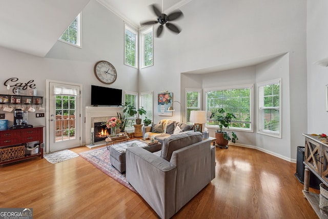 living area with ceiling fan, a warm lit fireplace, a towering ceiling, wood finished floors, and baseboards