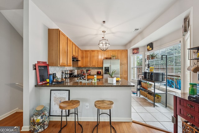 kitchen featuring appliances with stainless steel finishes, under cabinet range hood, a peninsula, decorative backsplash, and a sink