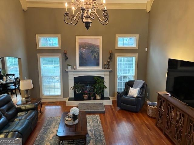 living room featuring a fireplace with raised hearth, crown molding, wood finished floors, a chandelier, and baseboards