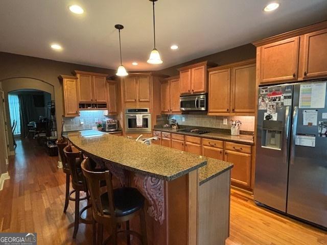 kitchen with stainless steel appliances, arched walkways, light wood finished floors, tasteful backsplash, and recessed lighting