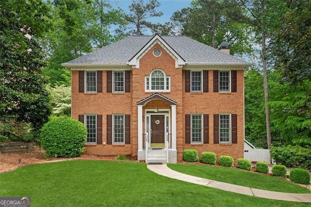 view of front of property featuring brick siding, a front yard, a chimney, and a shingled roof