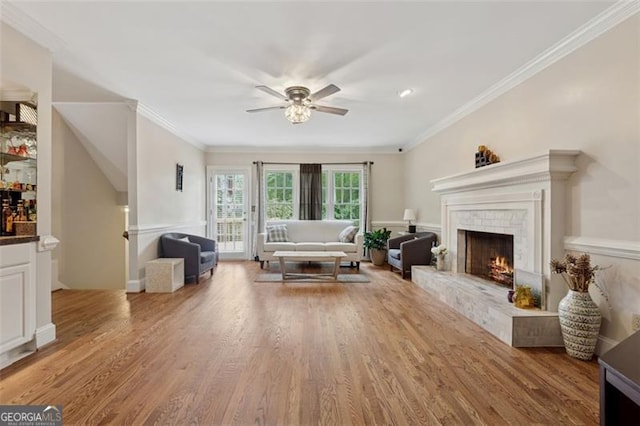 living room featuring a ceiling fan, light wood-style flooring, crown molding, and a brick fireplace
