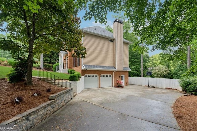view of side of property with concrete driveway, a chimney, a garage, fence, and brick siding