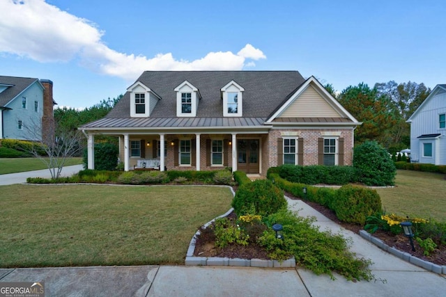 cape cod home featuring a standing seam roof, covered porch, a front lawn, and brick siding