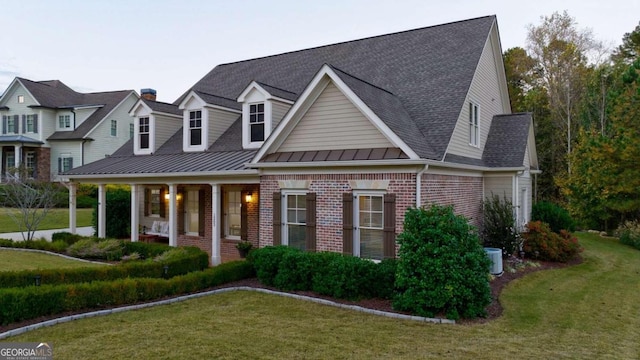 view of front facade with brick siding, a shingled roof, a front yard, and a standing seam roof