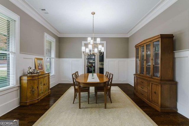 dining room featuring dark wood-style flooring, a decorative wall, a chandelier, crown molding, and wainscoting