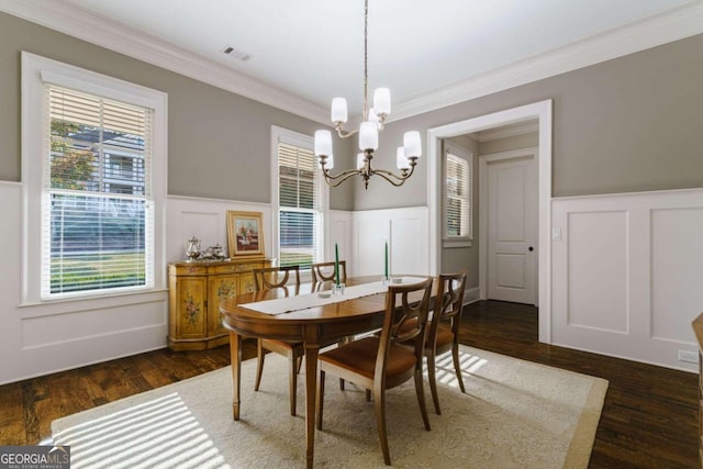 dining area featuring a decorative wall, crown molding, a wainscoted wall, a chandelier, and wood finished floors