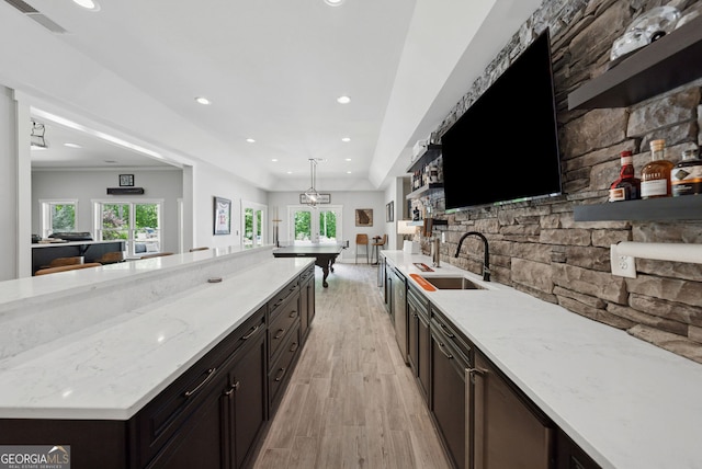 kitchen featuring a sink, open shelves, light wood-style flooring, light stone counters, and healthy amount of natural light