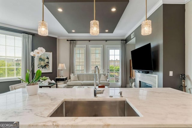 kitchen with a sink, crown molding, open floor plan, light stone countertops, and a premium fireplace