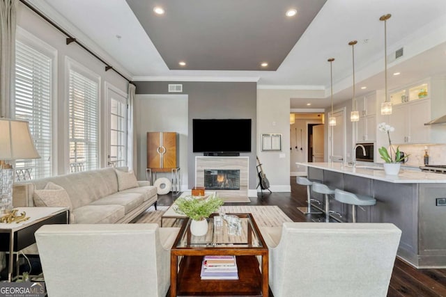 living area with dark wood-type flooring, baseboards, recessed lighting, ornamental molding, and a raised ceiling