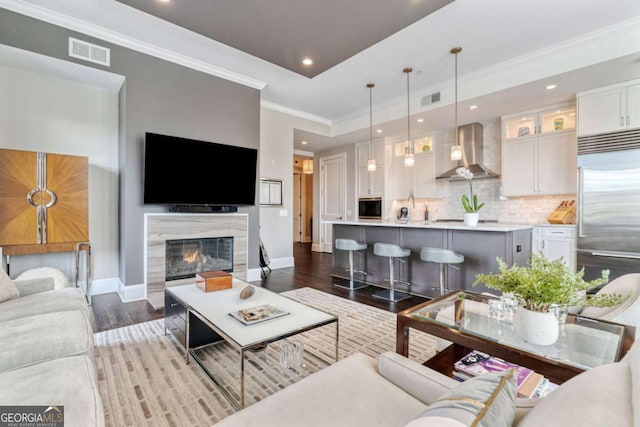 living room featuring baseboards, recessed lighting, wood finished floors, a high end fireplace, and crown molding