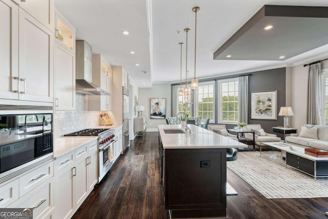 kitchen featuring high end appliances, wall chimney exhaust hood, a sink, dark wood-style floors, and recessed lighting