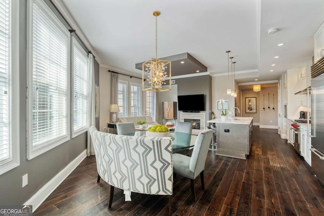 dining room with a chandelier, dark wood-style flooring, crown molding, baseboards, and a glass covered fireplace
