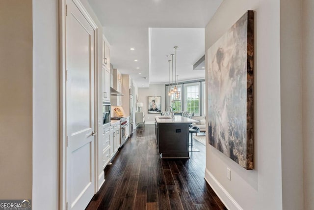kitchen with white cabinets, dark wood-style floors, light countertops, a center island with sink, and recessed lighting