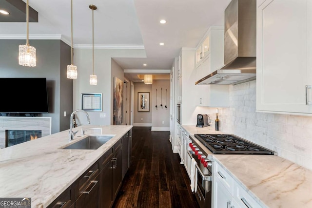 kitchen with appliances with stainless steel finishes, a sink, wall chimney range hood, light stone countertops, and dark wood finished floors