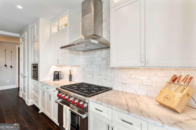 kitchen with wall chimney range hood, stainless steel stove, light stone countertops, white cabinets, and recessed lighting