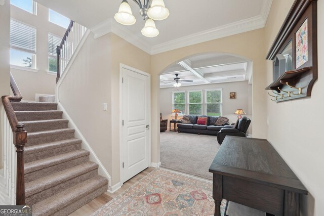 entryway featuring coffered ceiling, arched walkways, ceiling fan, a chandelier, and stairs