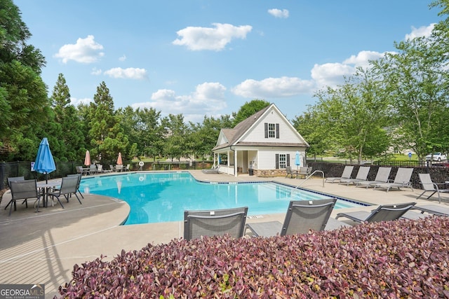 community pool with fence, a patio area, and view of wooded area