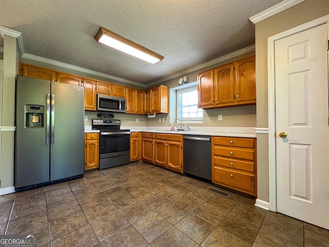 kitchen featuring appliances with stainless steel finishes, a sink, light countertops, crown molding, and a textured ceiling