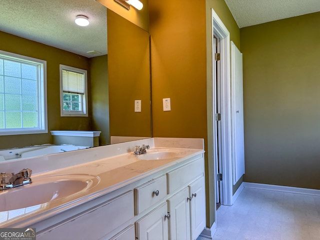 bathroom featuring a textured ceiling, tile patterned floors, baseboards, double vanity, and a tub to relax in
