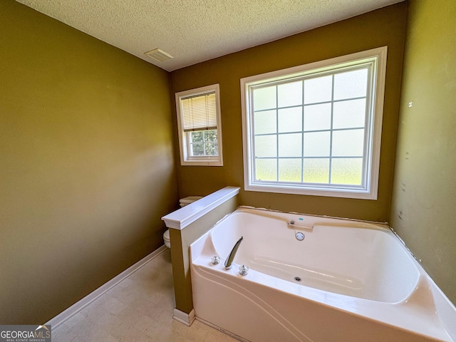 bathroom with a bath, toilet, baseboards, and a textured ceiling