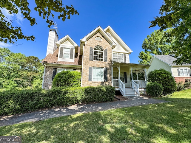 traditional-style home featuring a porch, a chimney, a front lawn, and brick siding