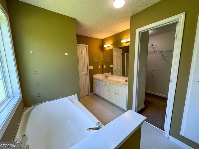 bathroom with a textured ceiling, a tub, double vanity, and baseboards