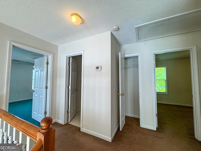 corridor featuring attic access, carpet floors, baseboards, and a textured ceiling