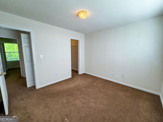 unfurnished bedroom featuring carpet flooring, a textured ceiling, baseboards, a spacious closet, and a closet