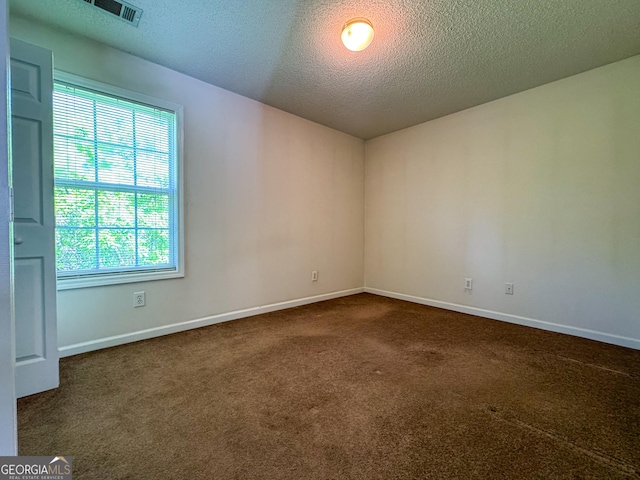 empty room with dark colored carpet, a textured ceiling, and baseboards