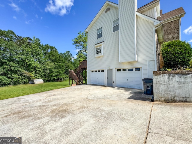 view of side of property featuring a garage, concrete driveway, stairs, a chimney, and a lawn