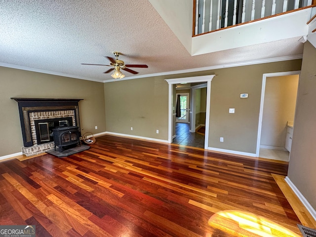 unfurnished living room with wood finished floors, a wood stove, a ceiling fan, ornamental molding, and a textured ceiling