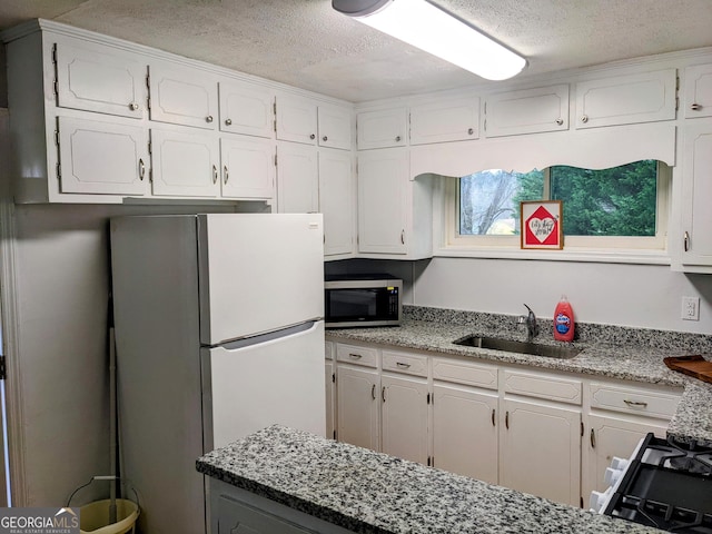 67 Sprayberry Rd, Newnan, GA 30263 - kitchen featuring freestanding refrigerator, stainless steel microwave, a sink, a textured ceiling, and white cabinetry
