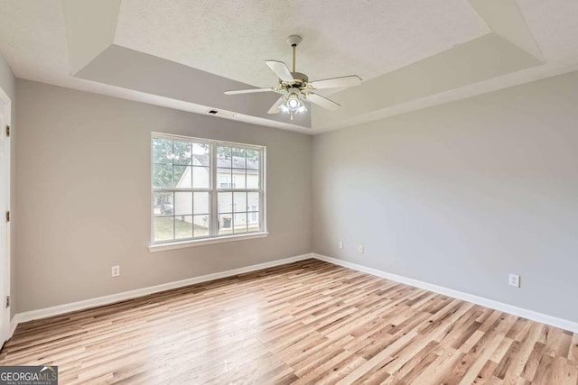 spare room with a raised ceiling, light wood finished floors, baseboards, and a textured ceiling