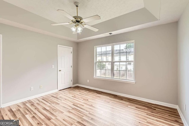 empty room featuring wood finished floors, baseboards, a tray ceiling, and a ceiling fan