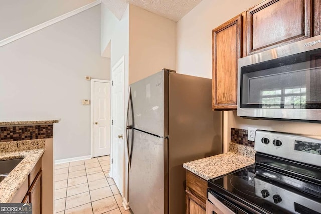 kitchen with stainless steel appliances, light tile patterned floors, and brown cabinets