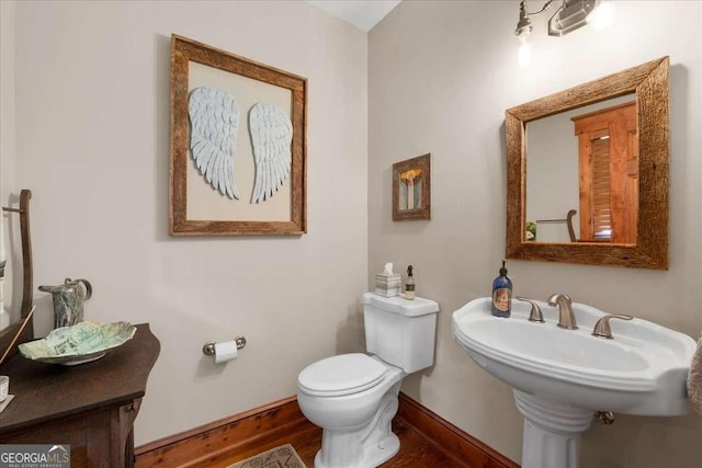 half bathroom with baseboards, toilet, and wood finished floors