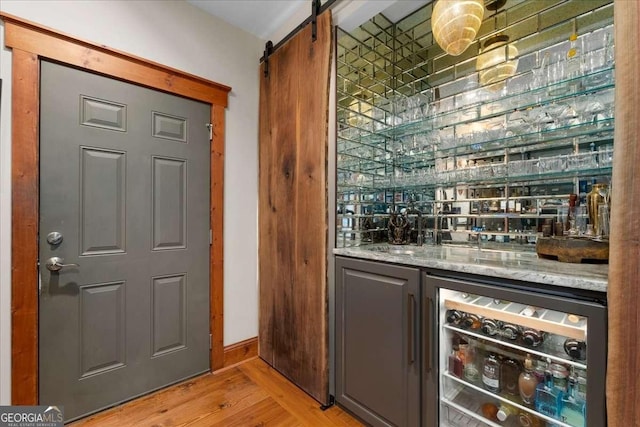 indoor wet bar with wine cooler, light wood-style flooring, a barn door, and baseboards
