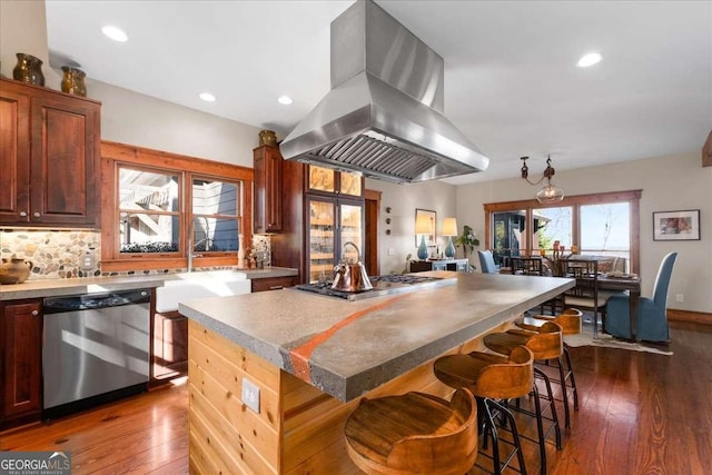 kitchen featuring appliances with stainless steel finishes, island range hood, dark wood-style flooring, a kitchen island, and tasteful backsplash