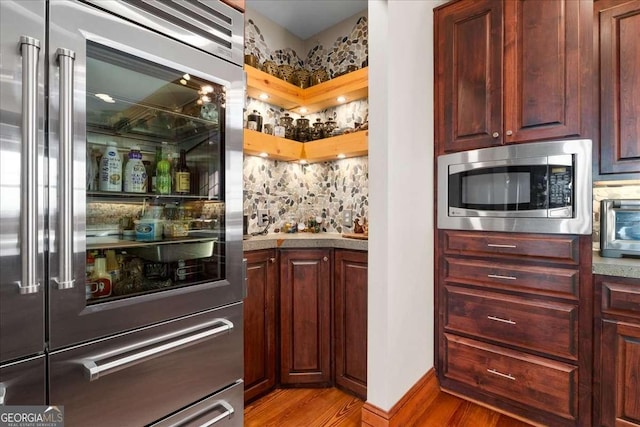 indoor bar featuring built in appliances, light wood finished floors, and tasteful backsplash